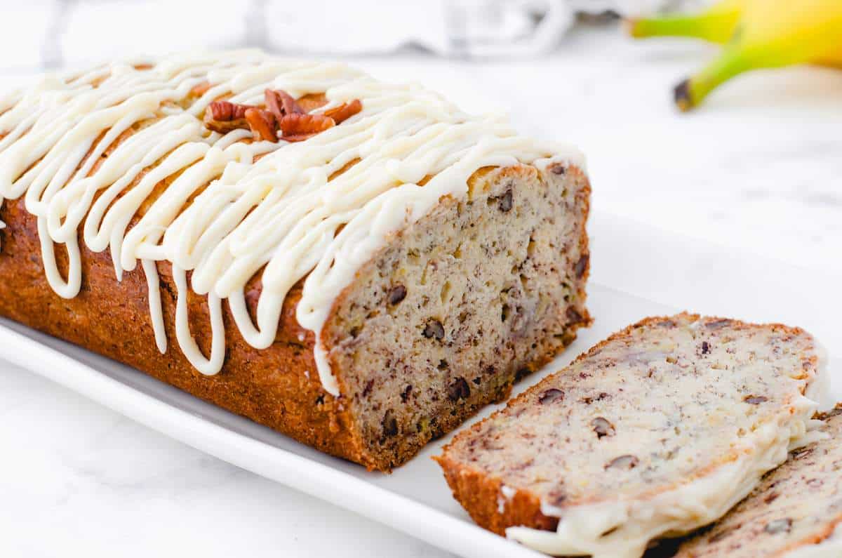 A loaf of buttermilk banana bread with cream cheese frosting drizzled over the top.