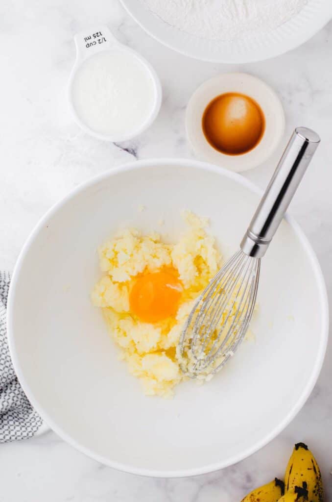 Eggs and butter being creamed in a white bowl.